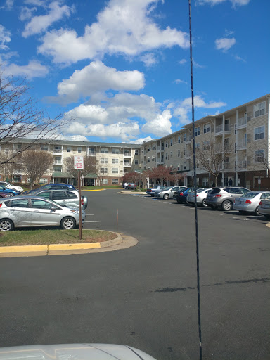 A view of a residential apartment complex with cars parked in the lot under a partly cloudy sky.