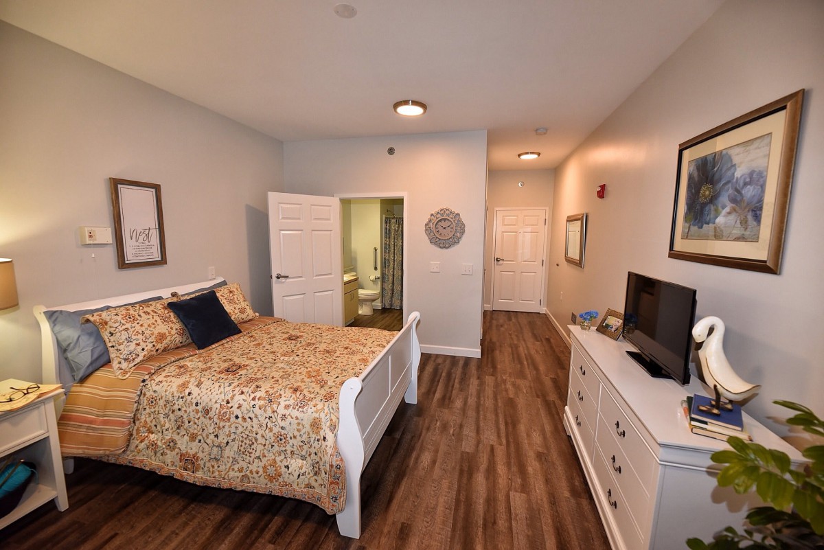 A cozy bedroom with a bed, television, and wooden flooring.