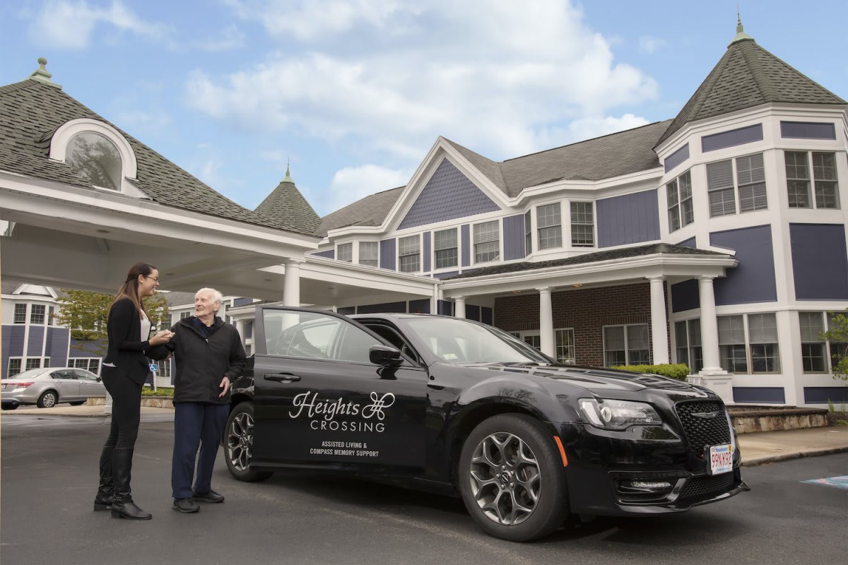 Two people standing next to a luxury car in front of a large building.
