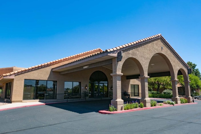 A commercial building entrance with an awning and adjacent parking lot under a clear blue sky.