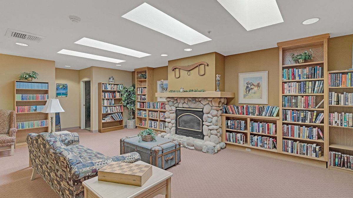 A cozy library room with a fireplace, surrounded by bookshelves and comfortable seating.