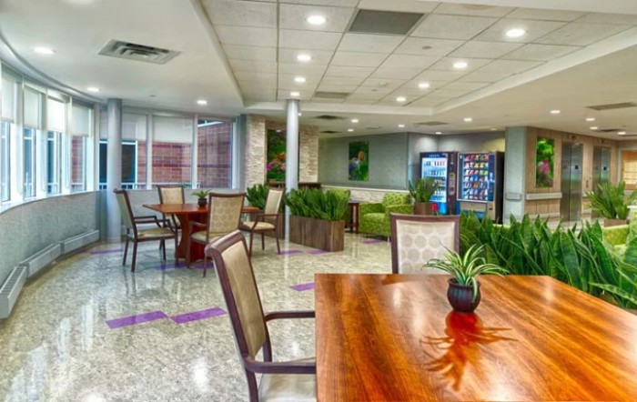 A modern lounge area with tables, chairs, and greenery.