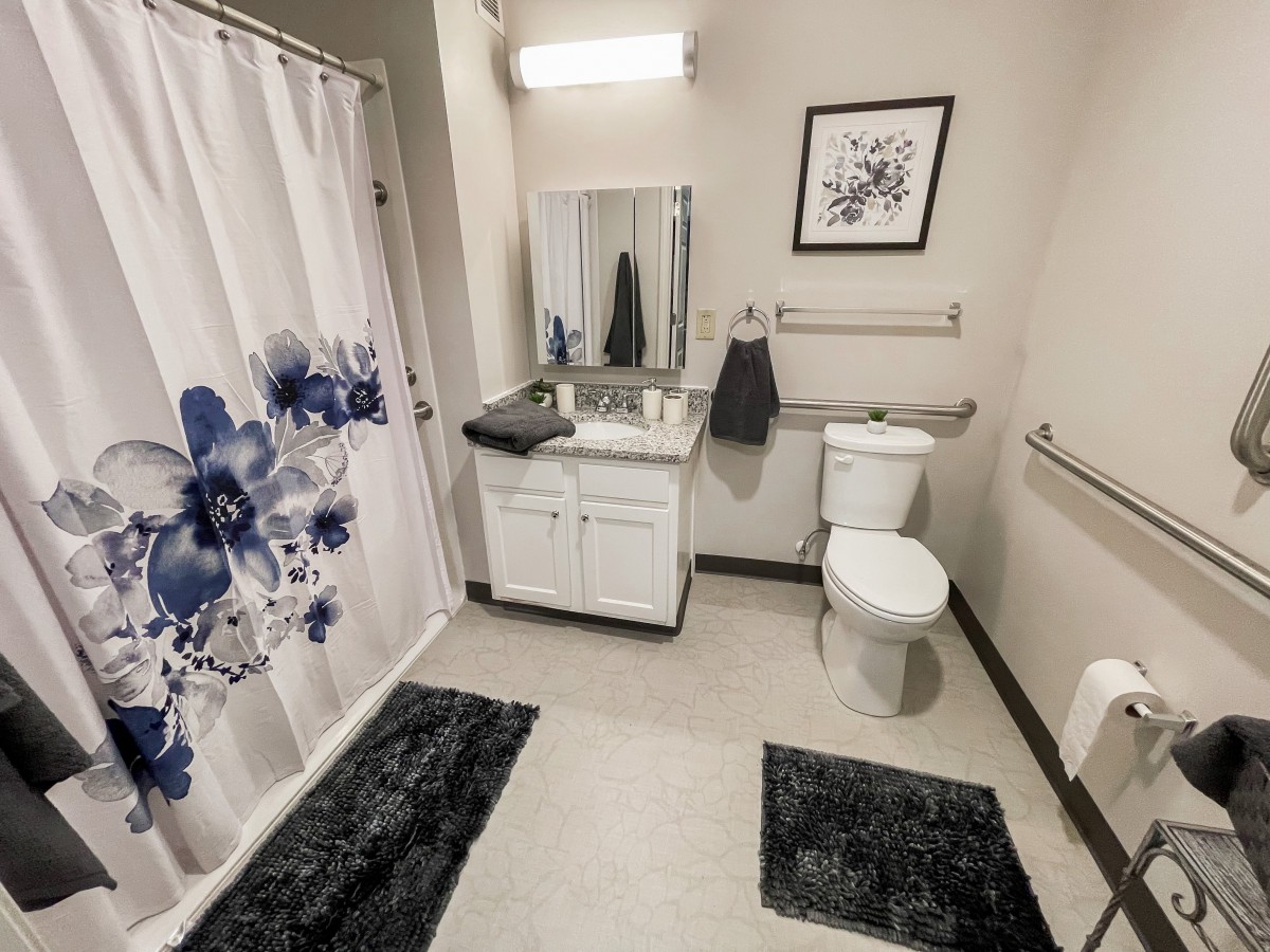A modern bathroom with a floral shower curtain, white vanity, and decorative touches.