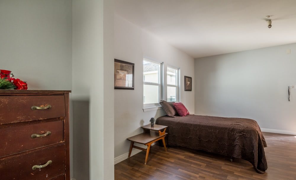 A cozy bedroom with a bed, wooden furniture, and natural light from the windows.
