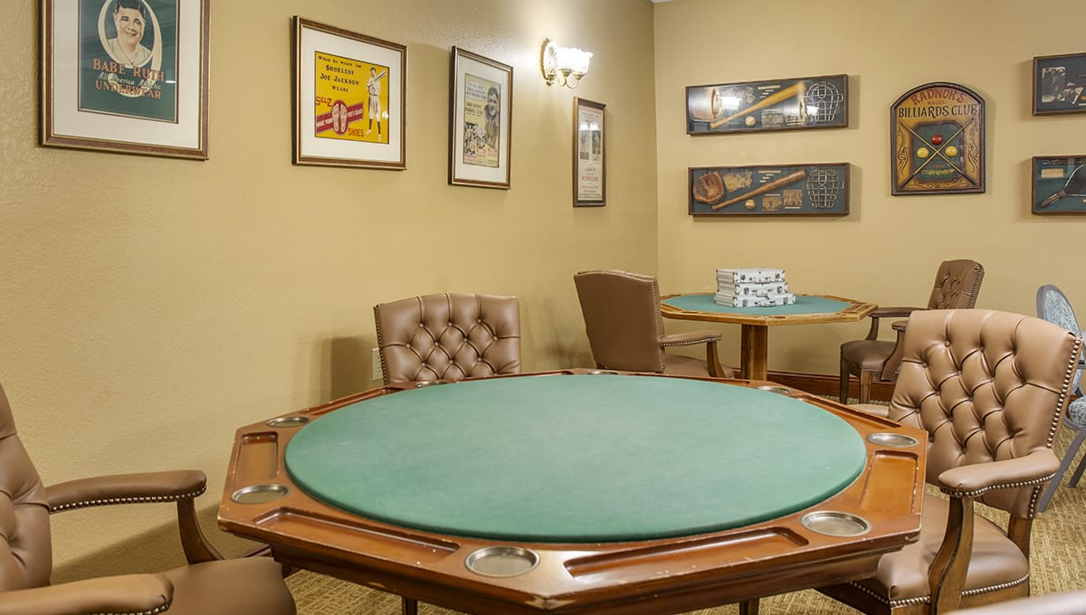 A cozy card room featuring a poker table and comfortable chairs, adorned with framed artwork on the walls.