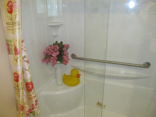 A cozy shower area featuring a rubber duck and a vase of flowers, with a glass door and grab bar.