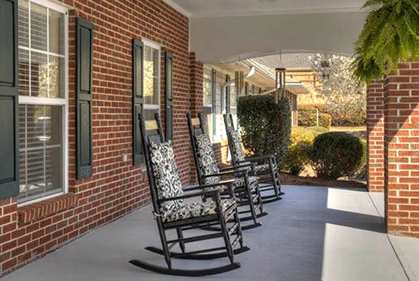 A cozy front porch with rocking chairs lined up against a brick wall.