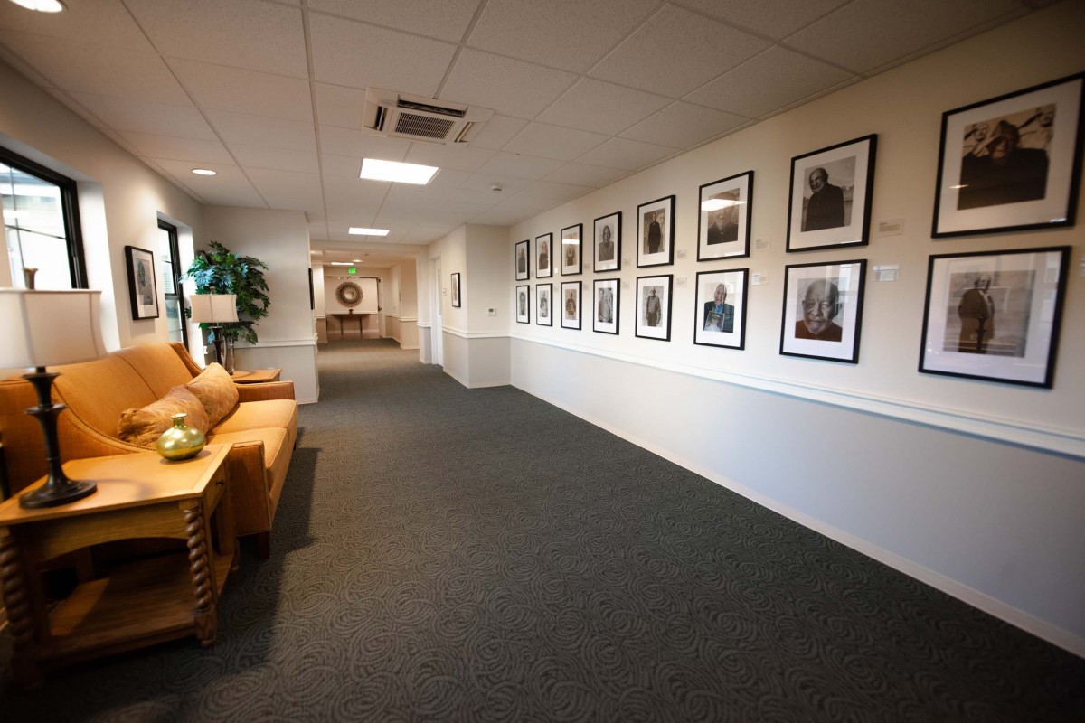 A well-lit hallway featuring a series of framed photographs on the wall and a wooden bench along the side.