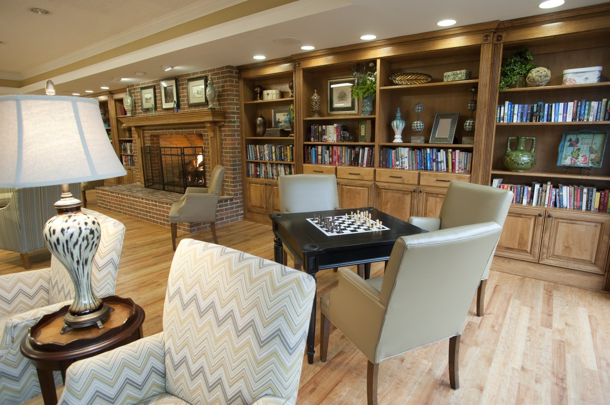 A cozy library with a fireplace, bookshelves, and a seating area featuring a chess table.
