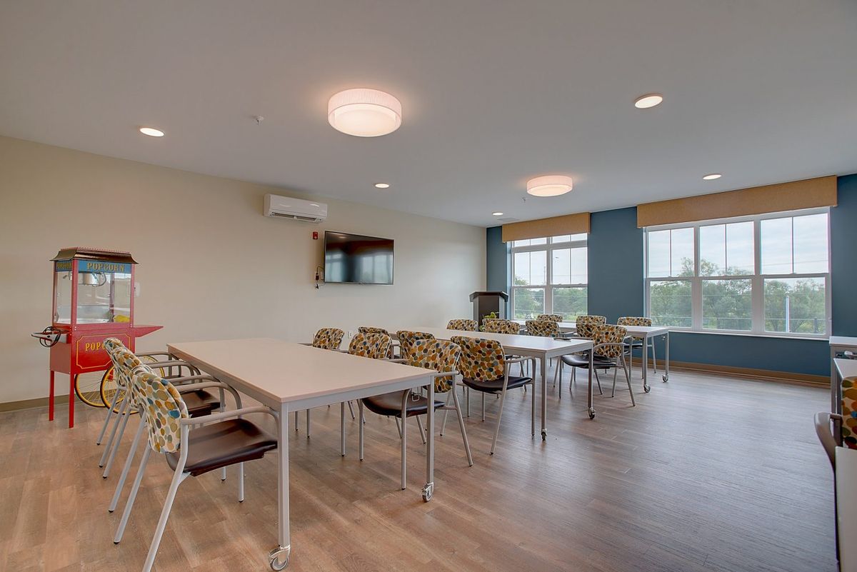 A modern classroom or meeting room with tables, chairs, and large windows.