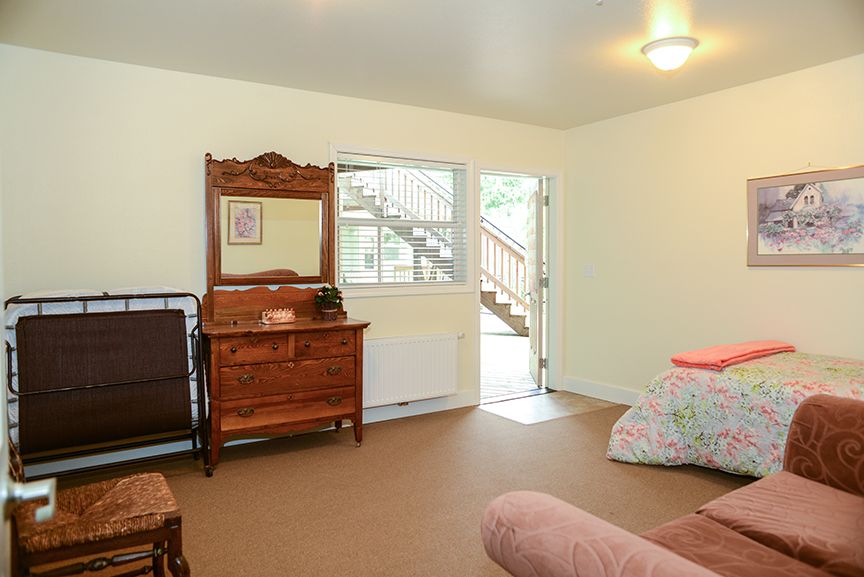 A bedroom interior with a vintage dresser, open door, and a bed.