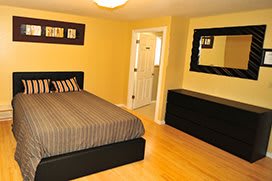 A neatly arranged bedroom with a bed, dresser, and mirror on a wooden floor.