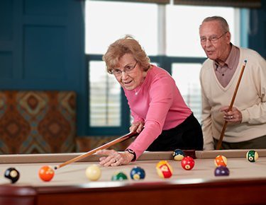 Two seniors enjoy a game of billiards together.