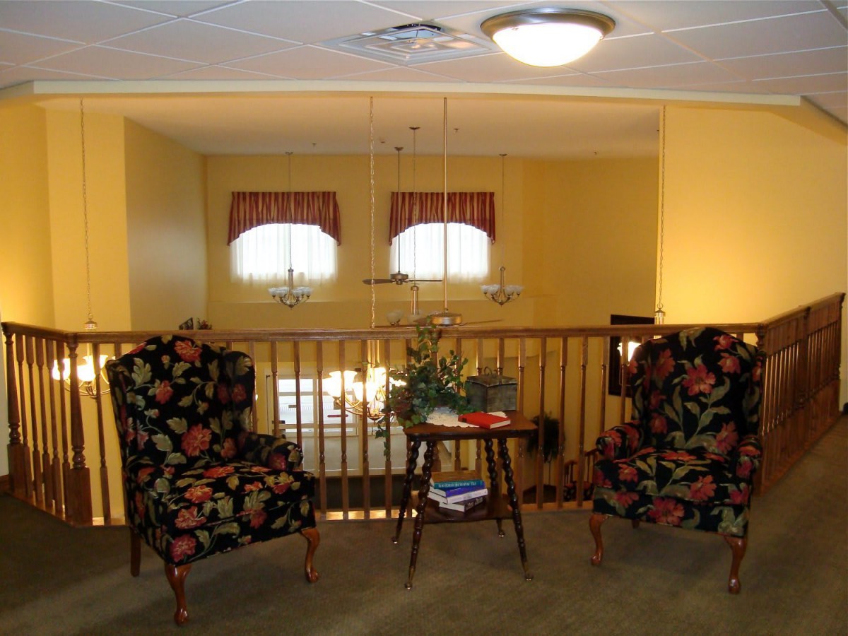 A cozy living room seating area with floral patterned chairs and a central wooden table, illuminated by ceiling lights.
