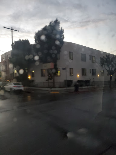 A rainy evening view of an urban building, reflecting the dim light from its windows.