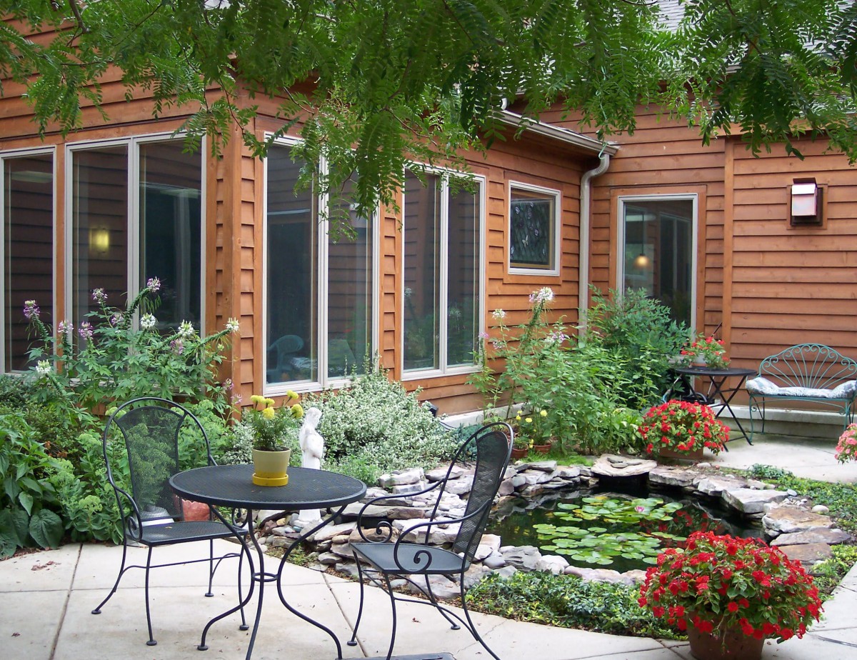 A cozy garden patio with a small pond surrounded by lush greenery and outdoor seating.