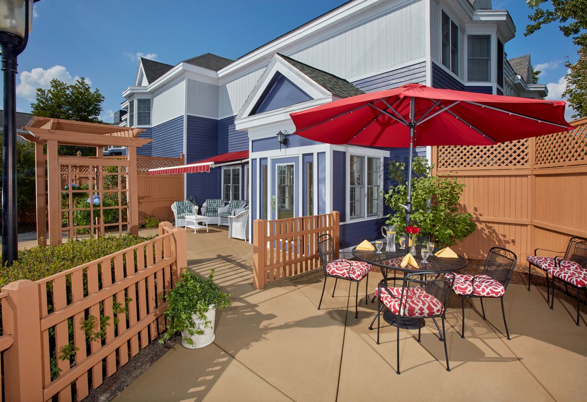 A cozy outdoor patio with red umbrellas and seating, set against a blue residential building.