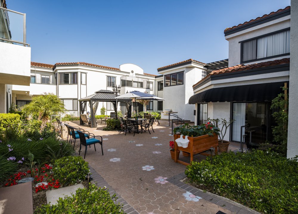 A modern apartment complex with a well-maintained outdoor patio and seating area surrounded by lush landscaping.