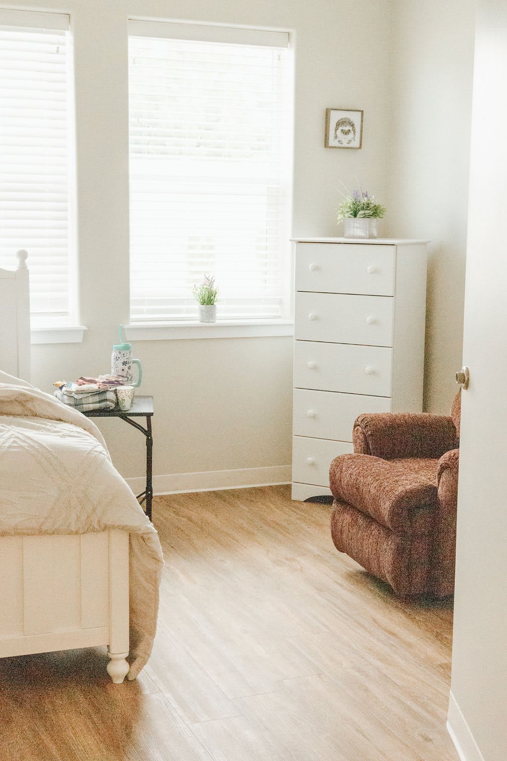 A cozy bedroom with a bed, chest of drawers, and an armchair.
