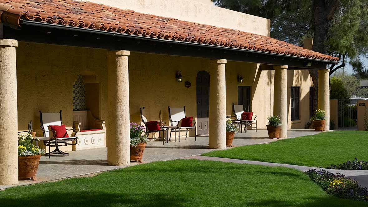 A Mediterranean-style veranda with columns and outdoor seating overlooking a well-manicured lawn.