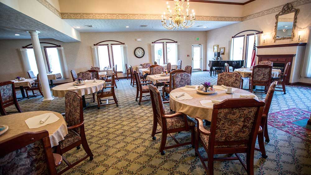 A spacious dining area with neatly arranged tables and chairs, featuring a chandelier and grand piano.