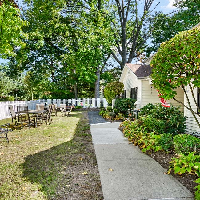 A serene garden with a paved pathway surrounded by lush greenery and outdoor seating.