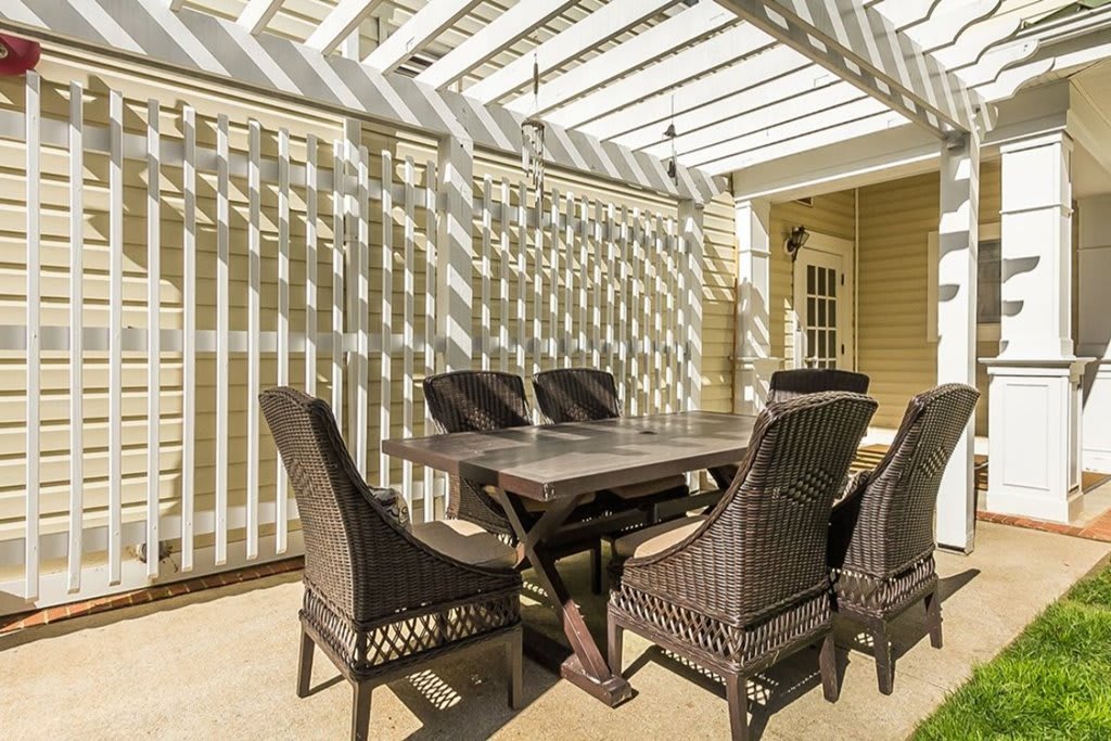 A sunlit patio with a pergola casting shadows on an outdoor dining set.