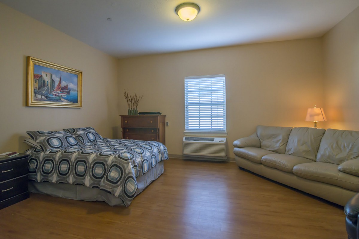 A cozy bedroom with a bed, sofa, and wooden flooring.