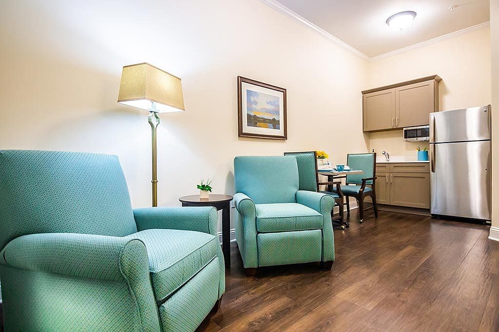 A cozy living room with teal armchairs, a table, and a standing lamp.