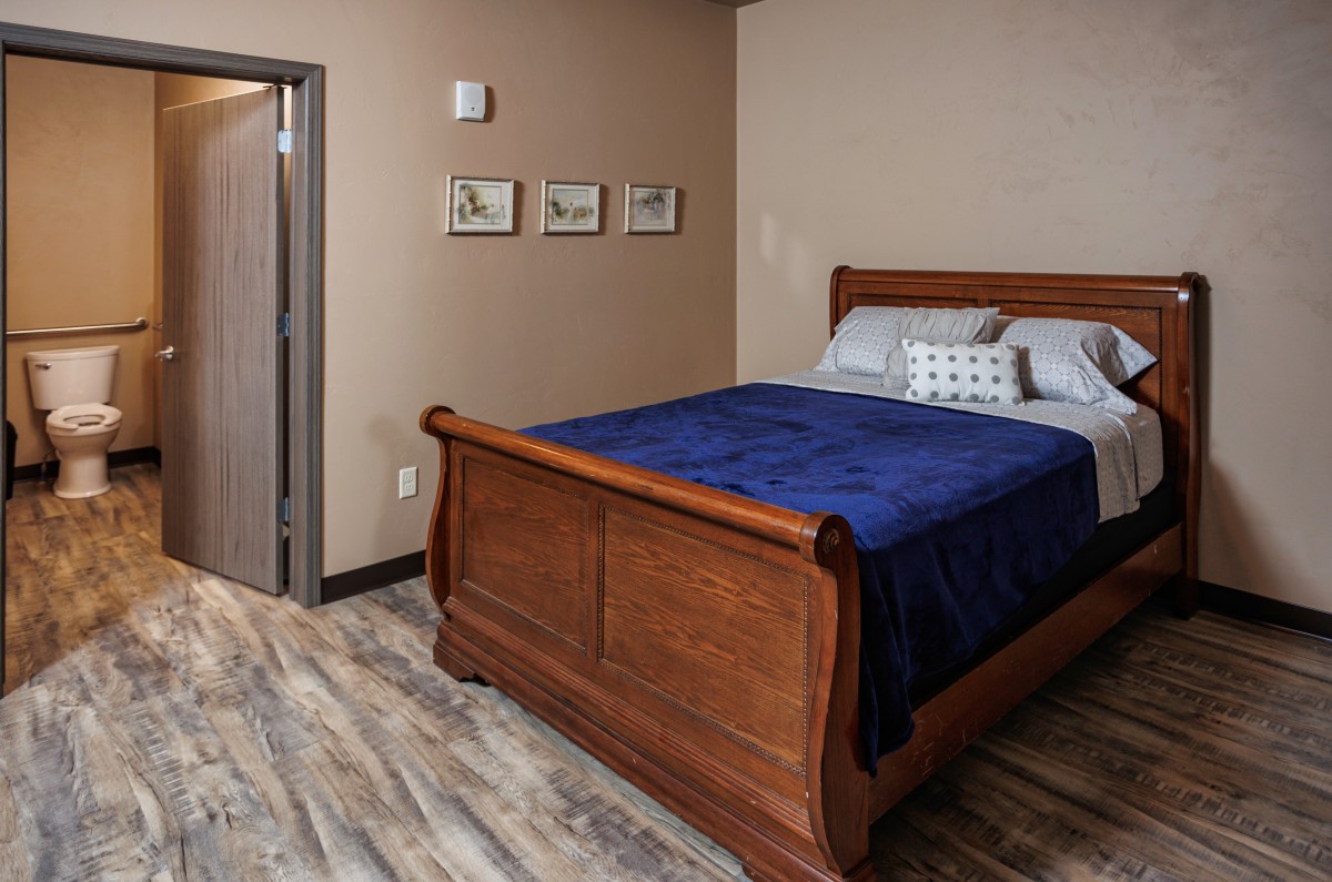 A cozy bedroom featuring a wooden sleigh bed with blue bedding, complemented by wall art and wood-style flooring.