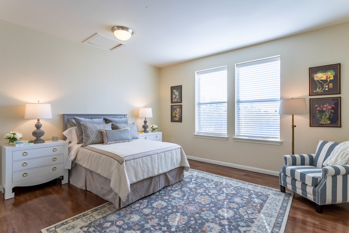A cozy bedroom with a neatly made bed, stylish rug, and ample natural light coming through the windows.