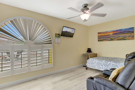A cozy and well-decorated bedroom featuring a ceiling fan, television, and artistic wall decor.