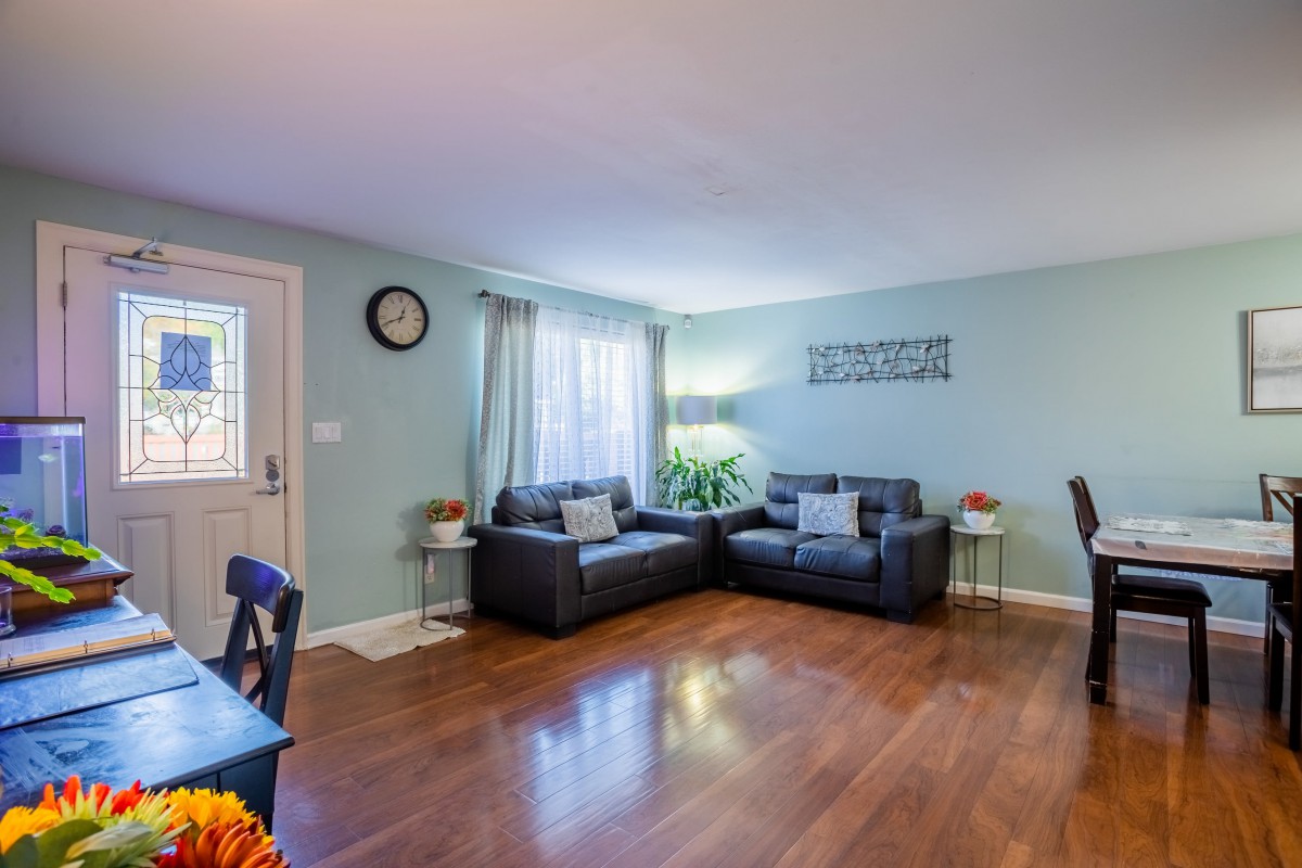 A cozy living room with a sectional sofa, hardwood flooring, and natural light from the window.