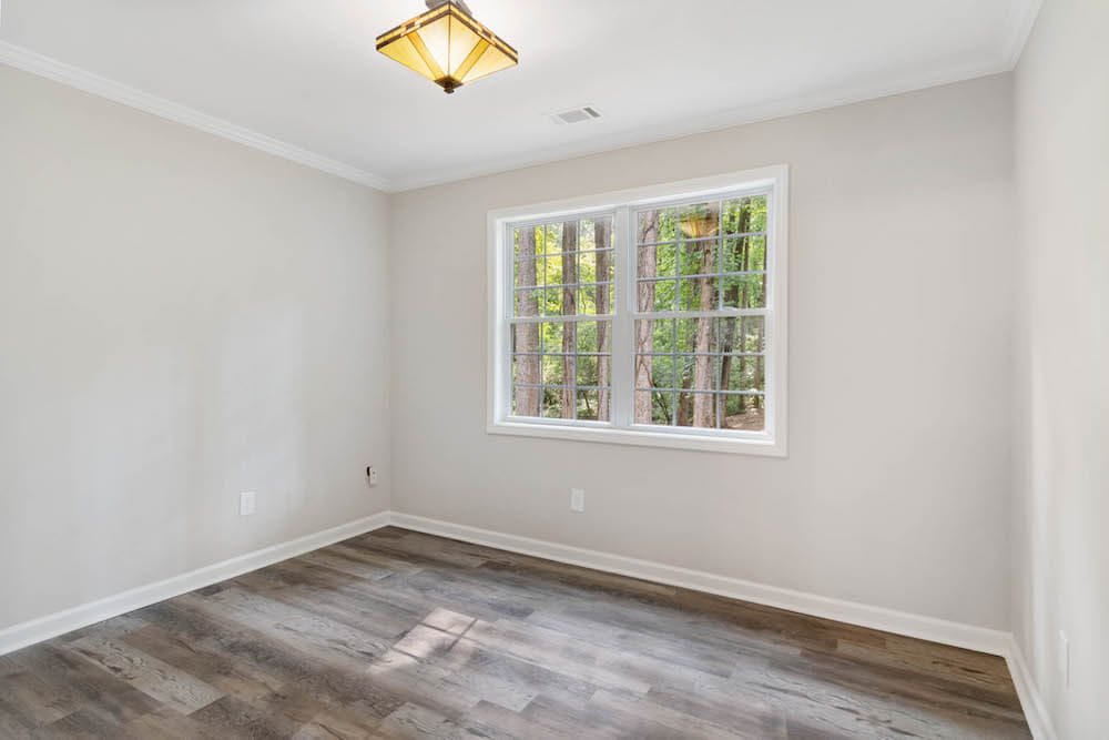 An empty room with wood flooring, white walls, and a large window letting in natural light.