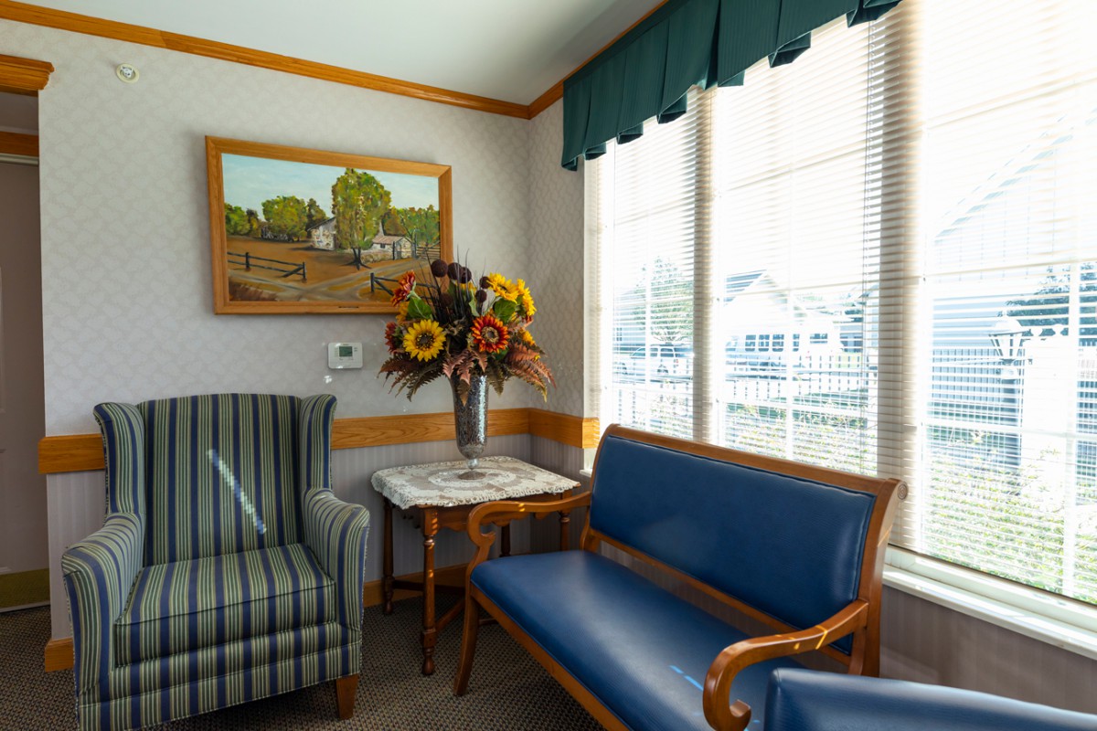 A cozy waiting room with comfortable seating, a vase of flowers, and a scenic painting.