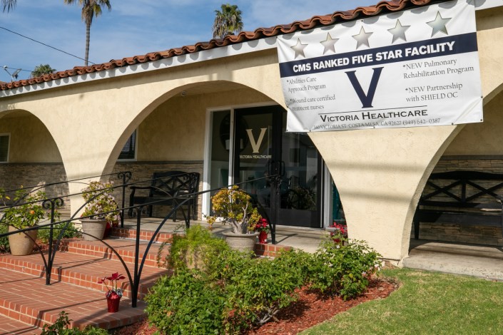 A healthcare clinic entrance with a banner displayed outside, surrounded by plants.