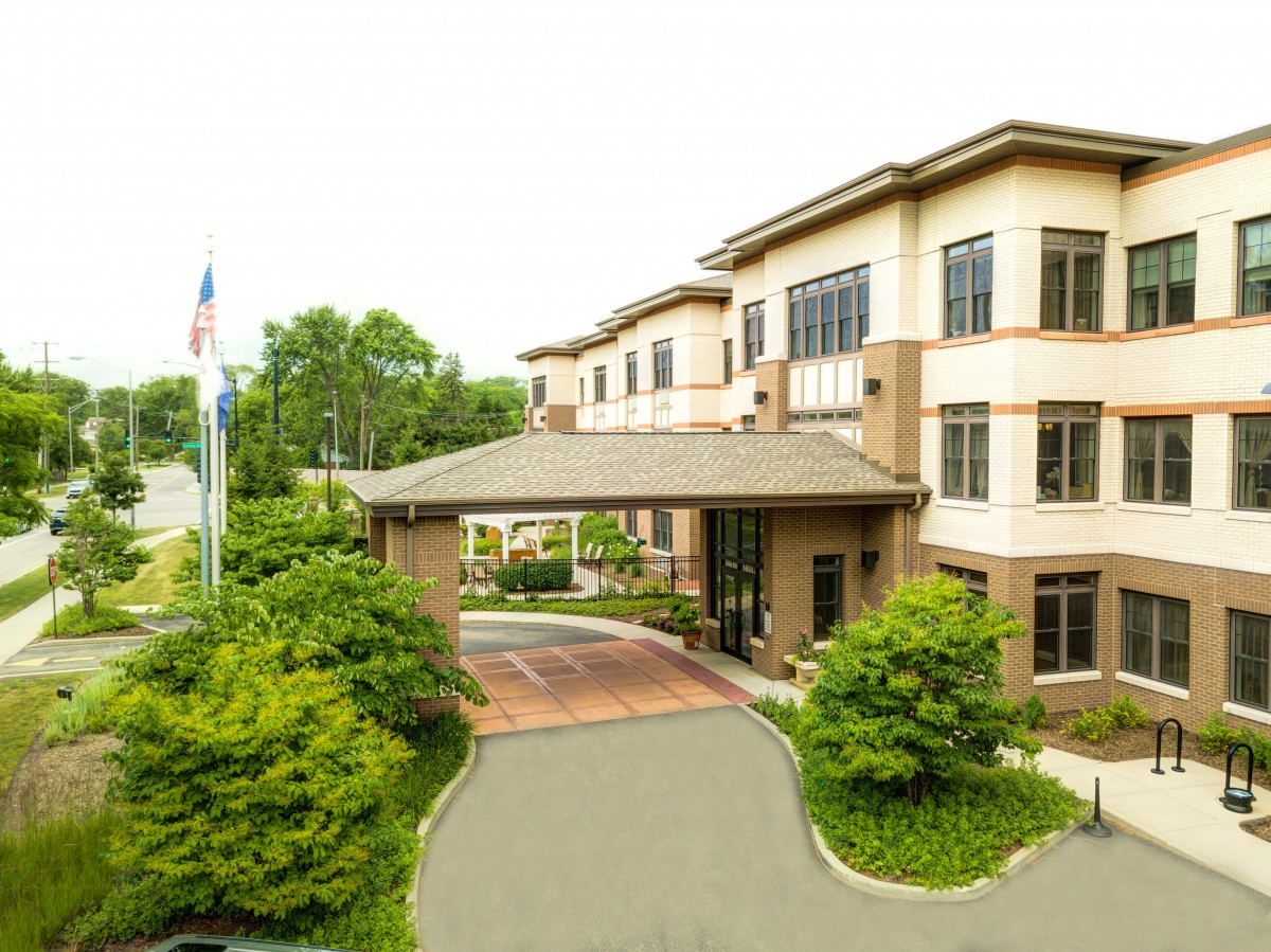A modern building with a covered entrance, surrounded by greenery and an American flag.