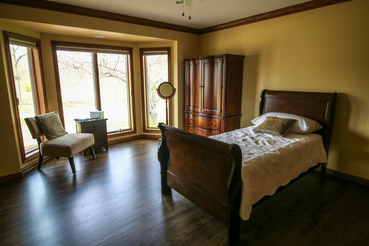 A cozy bedroom with a single bed, wooden wardrobe, and large window allowing natural light.