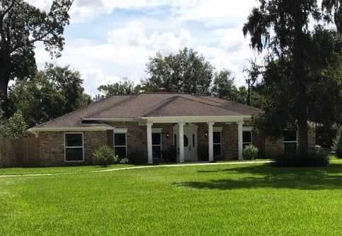 A brick house with a large lawn and front porch under a clear sky.