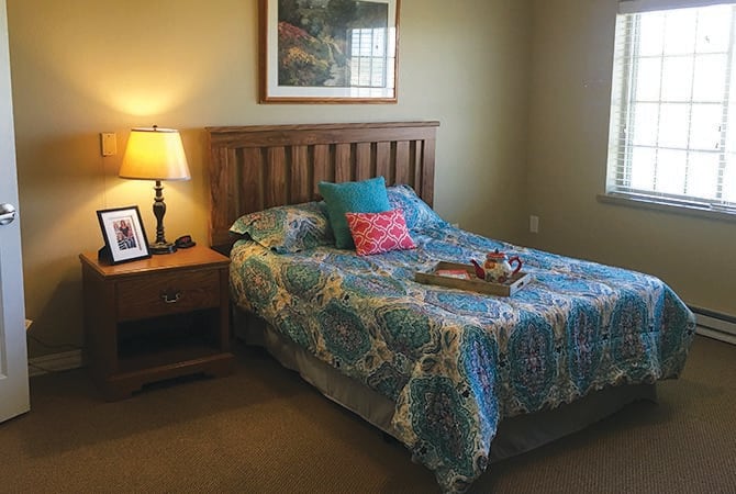 A cozy bedroom with a wooden bed frame, colorful bedding, and a warm lamp on the nightstand.