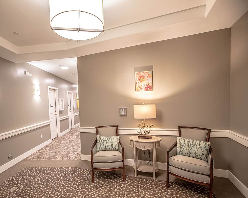 A cozy hallway with two chairs, a side table, and a lamp under soft ambient lighting.