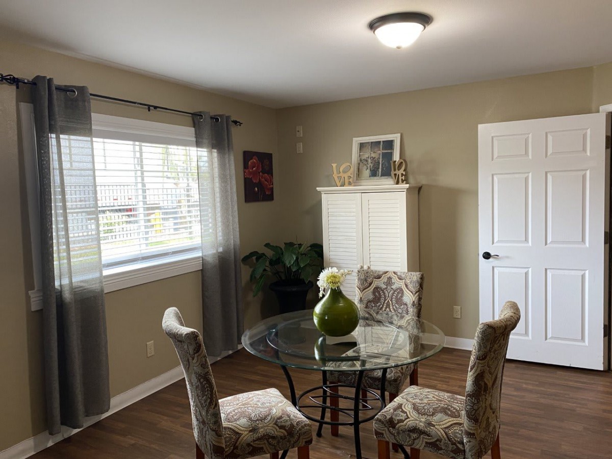 A cozy dining room featuring a glass-top table with ornate chairs, complemented by soft lighting and neutral decor.