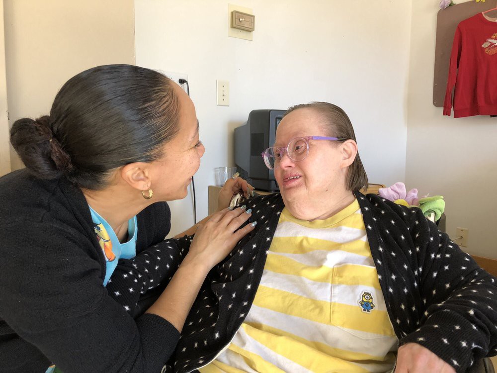 A caregiver interacting warmly with a person in a wheelchair, both smiling at each other.