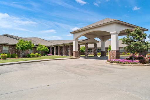 A welcoming entrance to a residential building, featuring well-maintained landscaping and a clear blue sky.