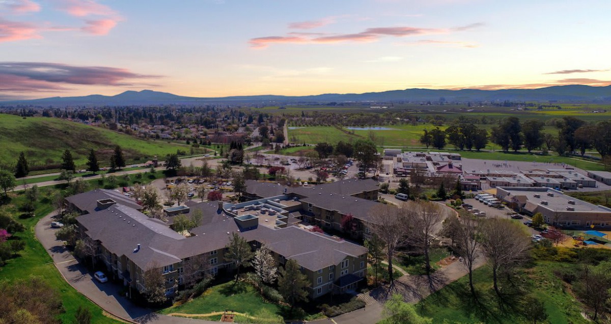 Aerial view of a residential area surrounded by greenery and mountains at sunset.