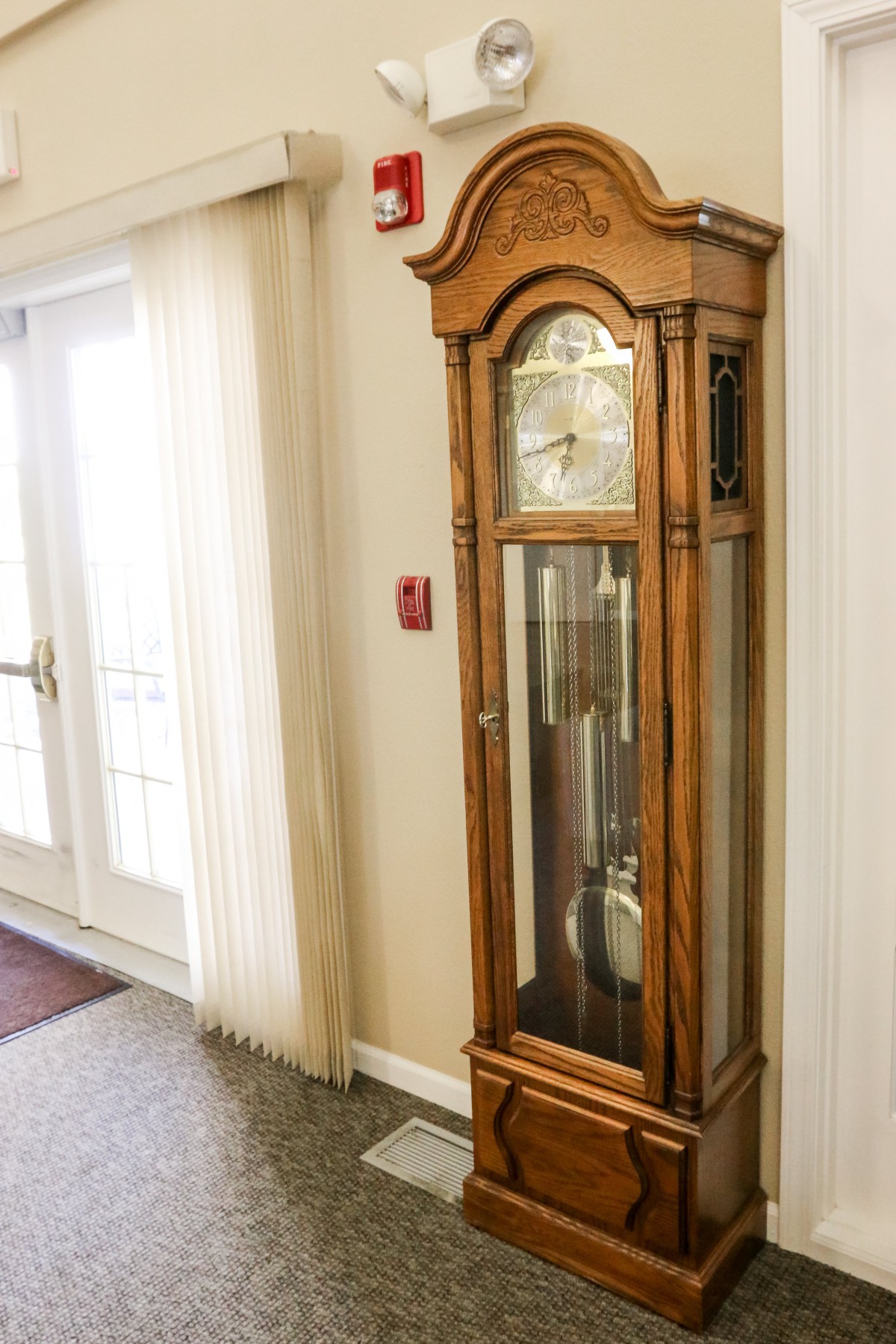 A classic wooden grandfather clock stands in a well-lit hallway.