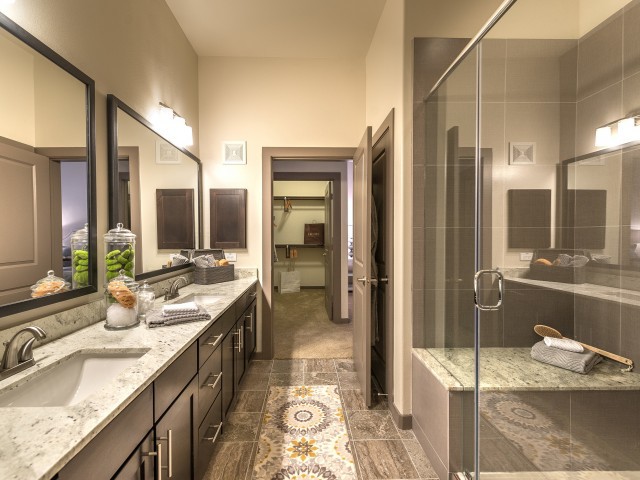 A modern bathroom with double vanity, large mirrors, and a glass-enclosed shower.