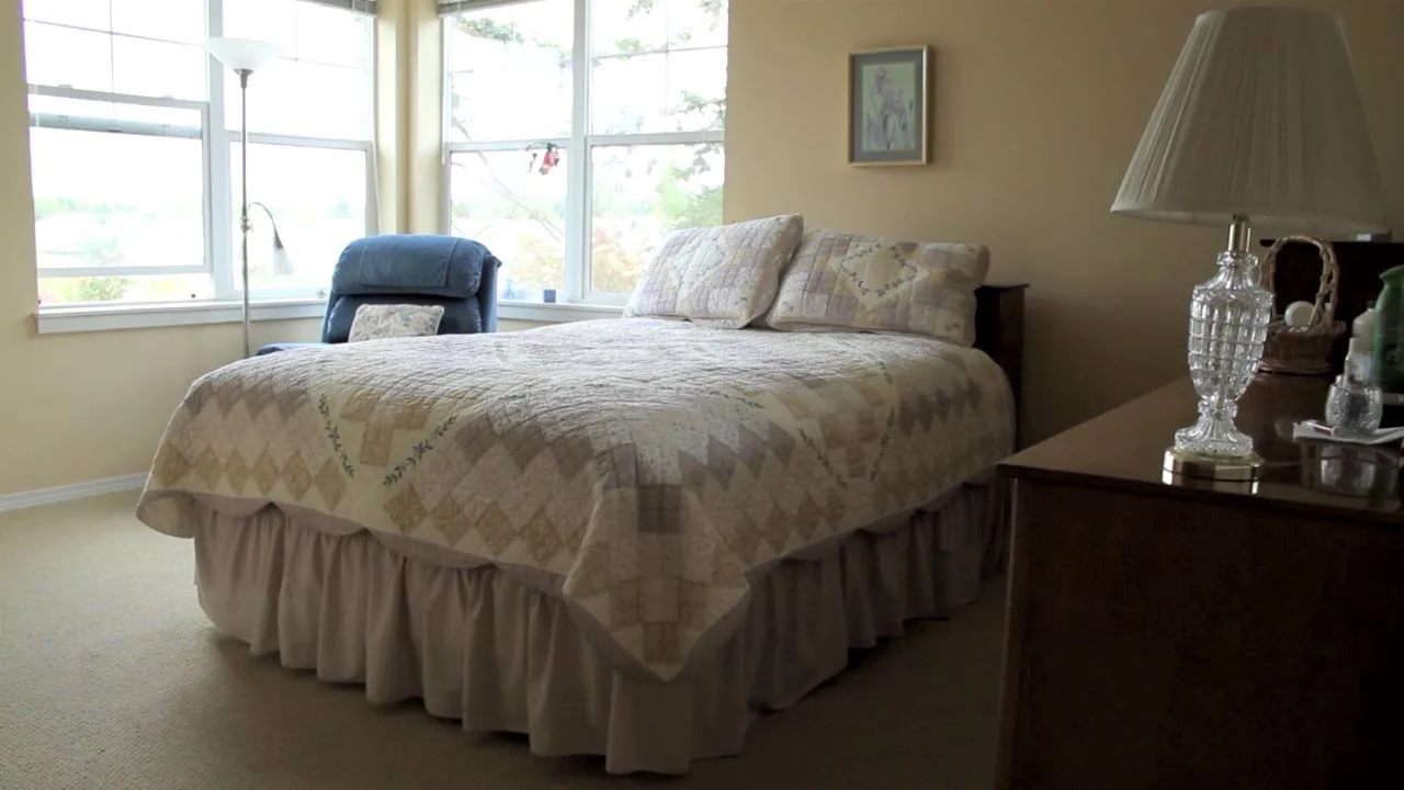A cozy bedroom with a neatly made bed and a chair by the window.