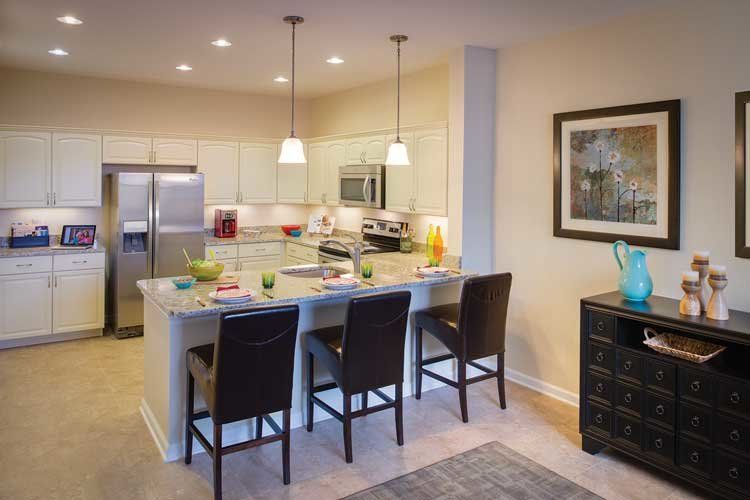 A modern kitchen with a large island, bar stools, stainless steel appliances, and pendant lighting.