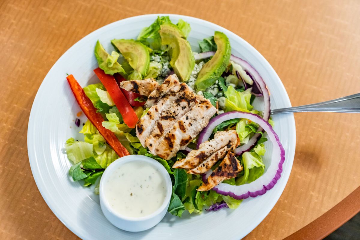 A fresh salad with grilled chicken, avocado, and a side of dressing.